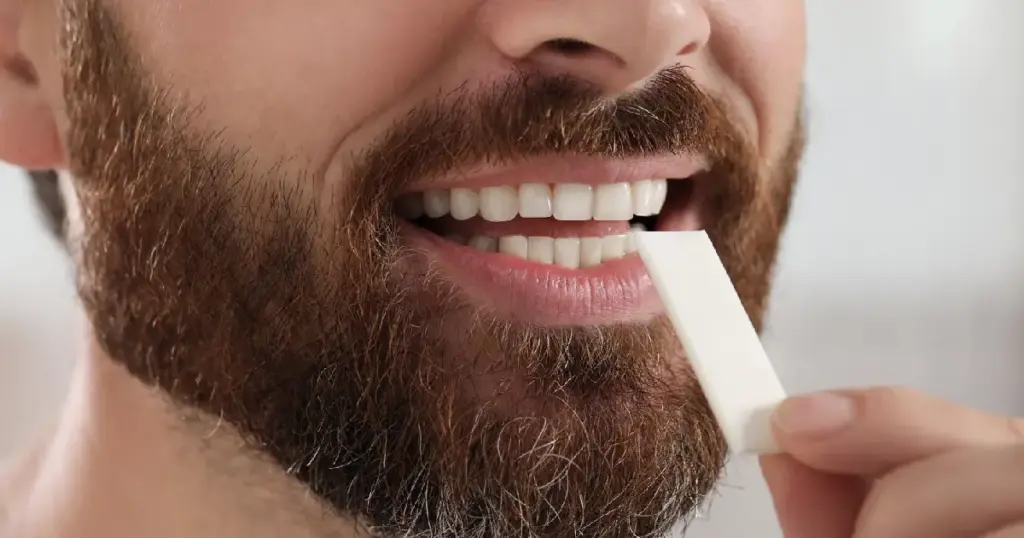 Man smiling with healthy teeth while holding gum, showing results of Dental Bridges in Annapolis.